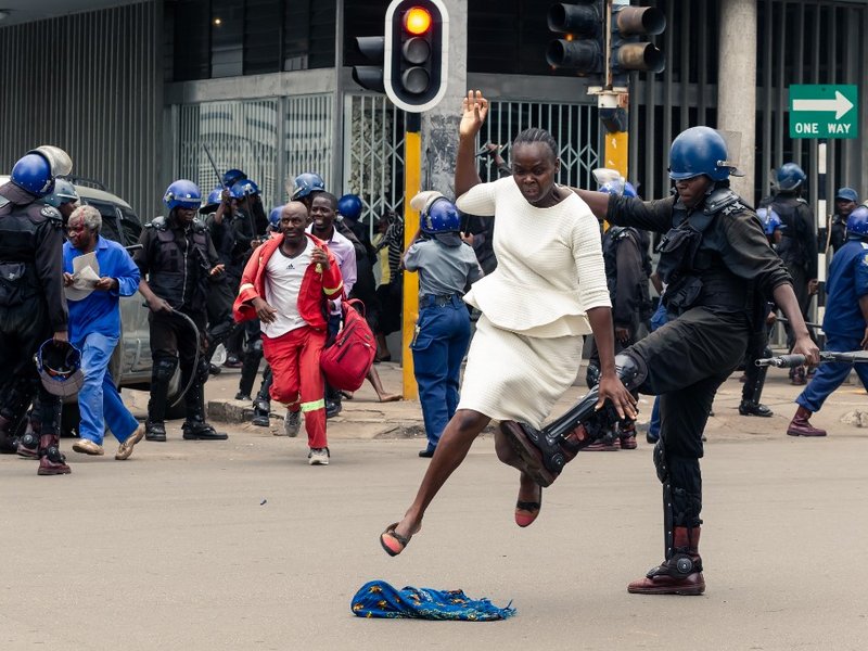 An anti-riot police man in Zimbabwe tackles a woman with his boot as they dispersed a crowd gathered to hear an address by leader of the MDC
