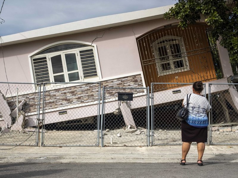 A woman stands in front of a house damaged by a 5.8 earthquake in Guanica, Puerto Rico on January 6, 2020.