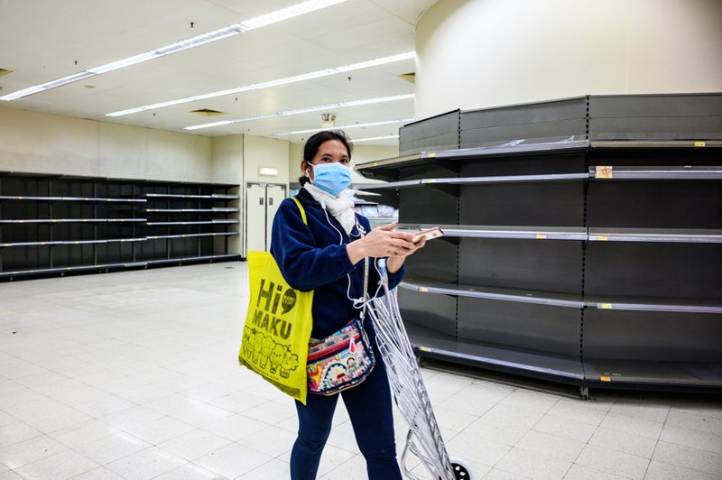 A shopper wearing a protective facemask walks past bare supermarket shelves, usually stocked with toilet paper and kitchen rolls, in Hong Kong on February 6, 2020. Panic buyers in Hong Kong have descended on supermarkets to snap up toilet paper after fals