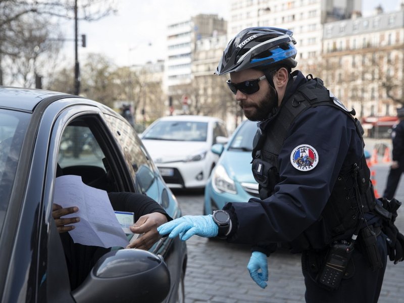 A French police officer checks that motorists are carrying the correct mobility document at the Place d'Italie in Paris, on March on 18, 2020. A strict lockdown requiring most people in France to remain at home came into effect at midday on March 17, 2020