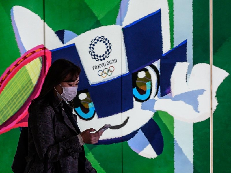 In this file photo taken on March 11, 2020 a woman wearing a face mask walks in the tunnel of a metro station with a poster of Miraitowa, official mascot of the 2020 Summer Olympics in Tokyo. Japan has asked for a one-year postponement of the Tokyo 2020 G