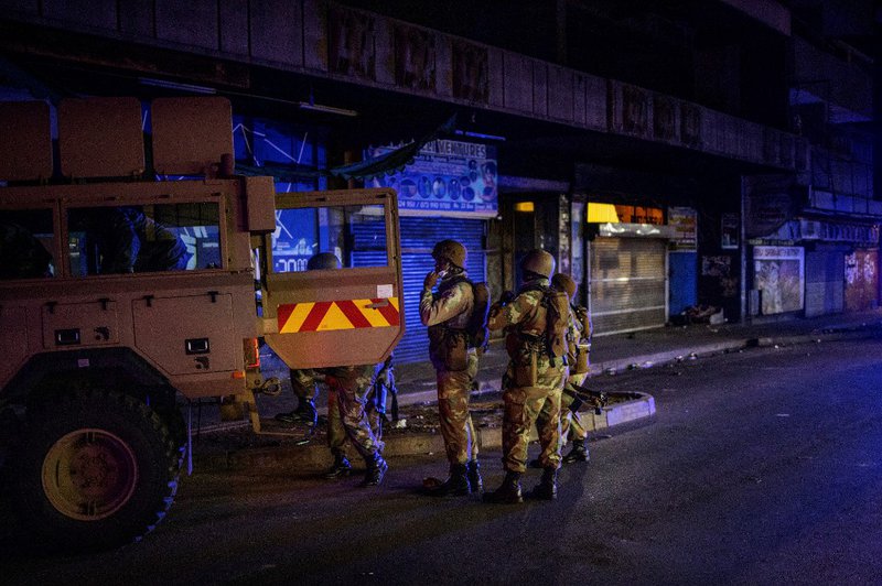 Members of the South African National Defence Force (SANDF) climb on an Armoured Personal Carrier (APC) during an operation in the Johannesburg CBD, on March 27, 2020. South Africa came under a nationwide military-patrolled lockdown on March 27, 2020, joi