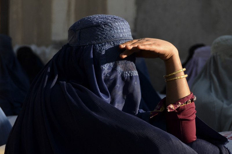 A burqa-clad woman waits with others outside a United Nations High Commissioner for Refugees (UNHCR) office as they wait to receive non-food items in Kandahar on March 8, 2022.