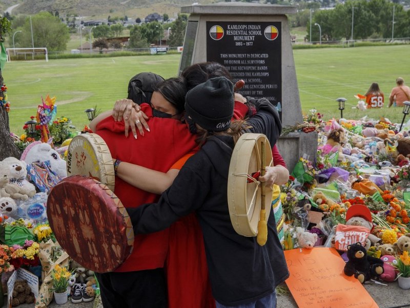 In this file photo taken on June 4, 2021, people from the Mosakahiken Cree Nation hug in front of a makeshift memorial at the former Kamloops Indian Residential School to honor the 215 children whose remains have been discovered buried near the facility,