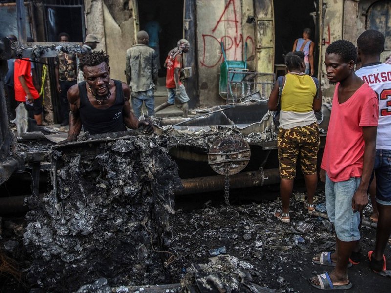 Men pick up aluminum pieces at the site where a tanker truck exploded in Cap-Haitien, Haiti, December 14, 2021. At least 62 people were killed when a gas tanker truck exploded in the Haitian city of Cap-Haitien on December 14, 2021 morning, a local offici
