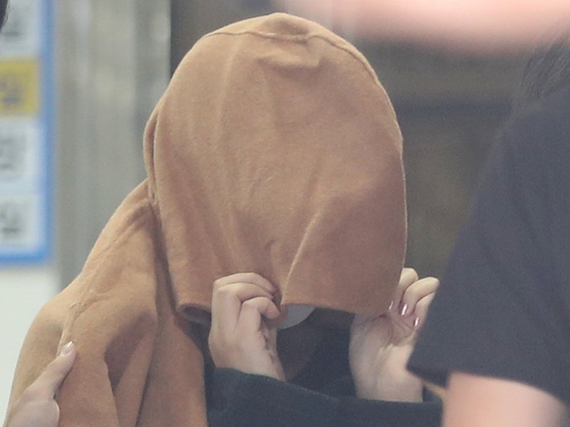 A 42-year-old woman, believed to be the mother of two children whose remains were found in suitcases in New Zealand, covers her head with a large brown coat at Ulsan Central Police Station after her arrest early morning in South Korea's southeastern city
