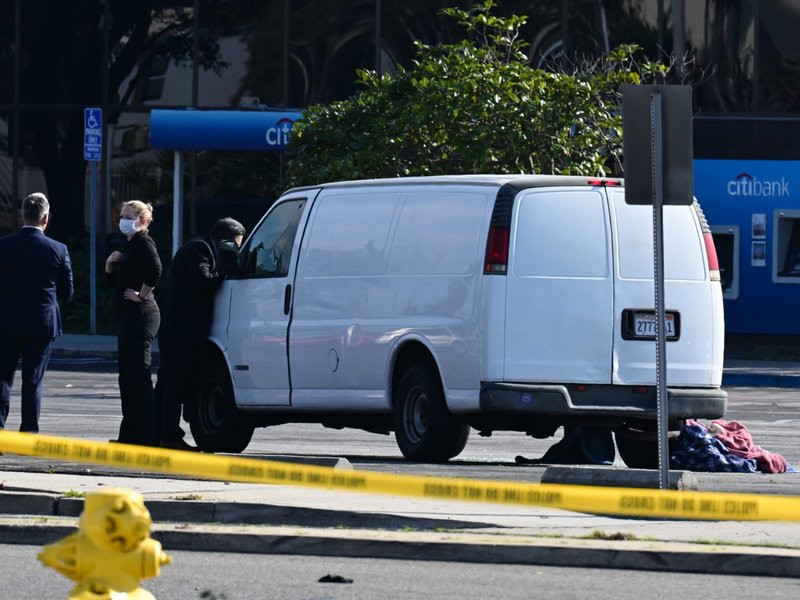 A law enforcement official looks into the window of a van with a body in the driver's seat in Torrance, California, on January 22, 2023.