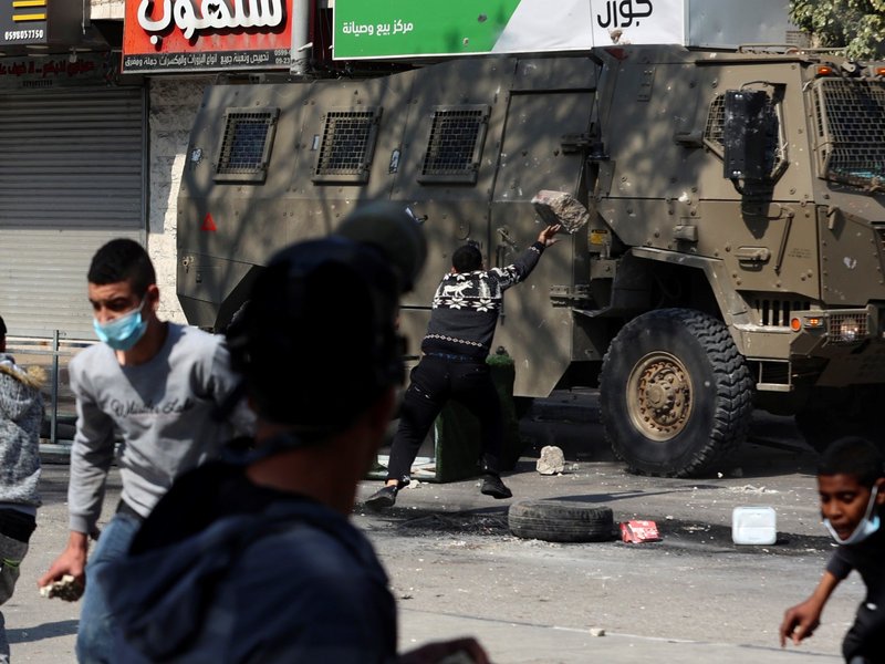 A Palestinian man tosses a rock against an Israeli military vehicle, during a raid on the occupied-West Bank city of Nablus, on February 22, 2023. Israeli troops killed at least 10 Palestinians in a raid on Nablus, while more than 80 suffered gunshot woun