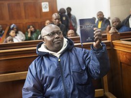 Fulgence Kayishema, one of the last fugitives sought for their role in the 1994 Rwanda genocide, holds up a Christian book as he sits in the Cape Town Magistrate's Court in Cape Town on May 26, 2023, two days after being arrested following 22 years on the