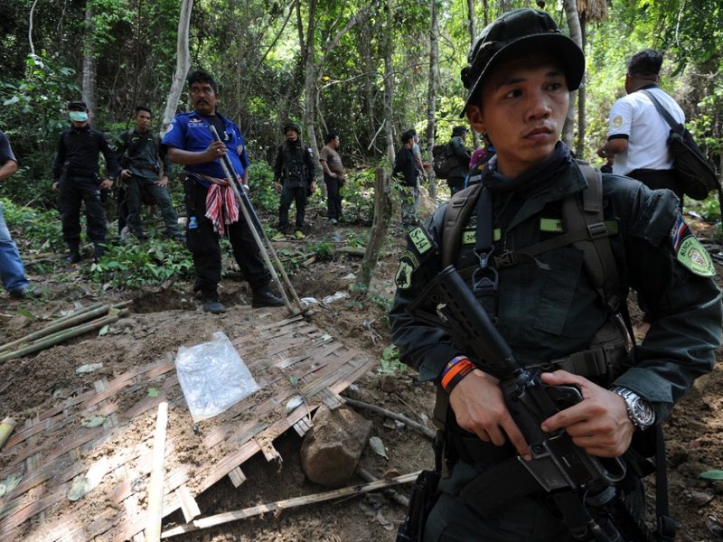 Soldiers stand guard as rescue workers and forensic officials dig out skeletons from shallow graves covered by bamboo at the site of a mass grave at an abandoned jungle camp in the Sadao district of Thailand's southern Songkhla province bordering Malaysia
