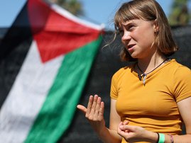 Swedish climate activist Greta Thunberg gestures while talking to media next to a Palestinian flag as a flotilla carrying humanitarian aid and activists prepare to leave for Gaza