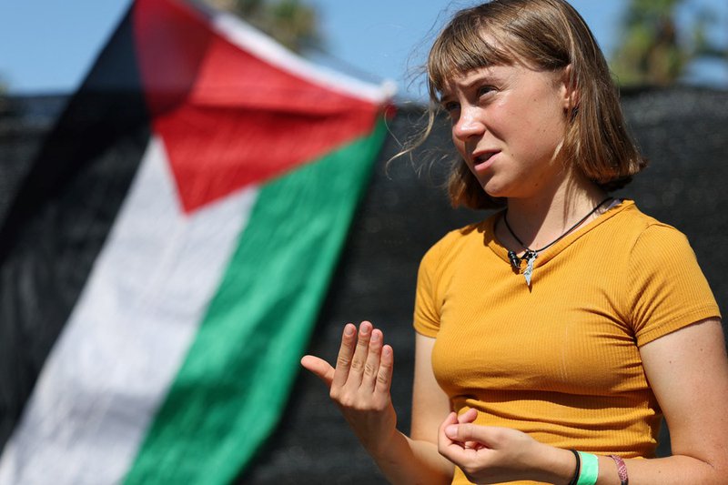 Swedish climate activist Greta Thunberg gestures while talking to media next to a Palestinian flag as a flotilla carrying humanitarian aid and activists prepare to leave for Gaza
