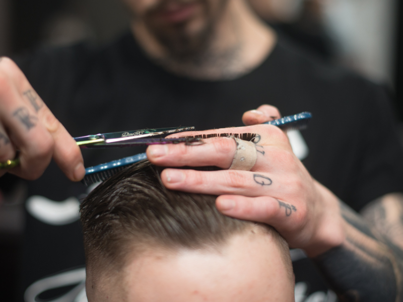 A barber is cutting a customer's hair with scissors