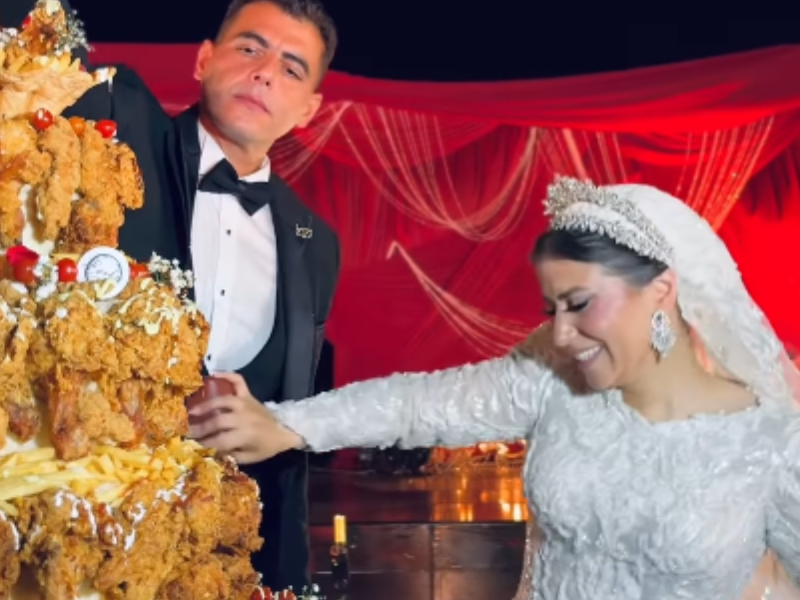 A bride and groom decorate their chicken wedding cake with sauce