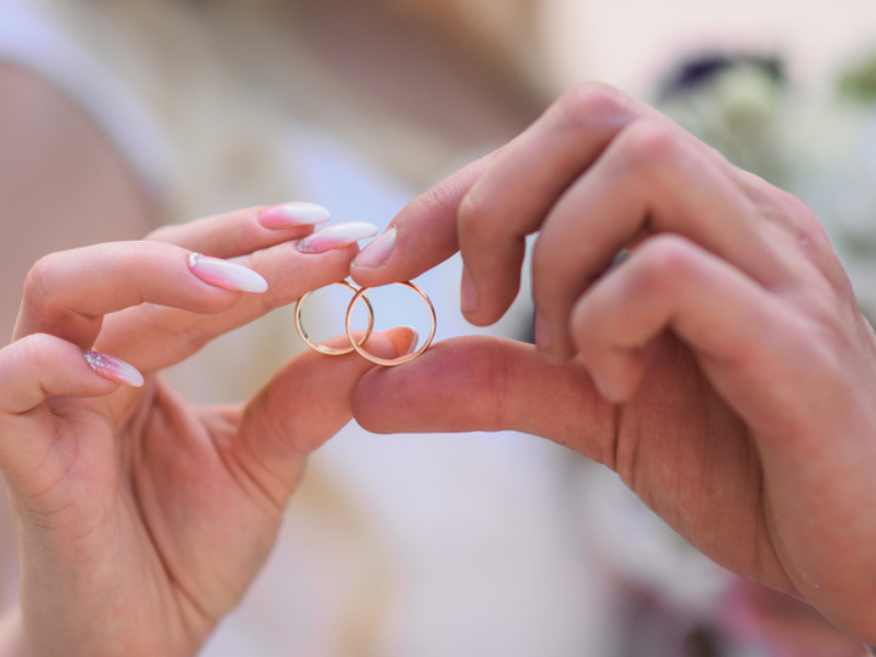 A bride and groom hold their wedding rings together