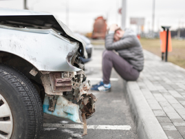 A broken car after an accident and man in background holding his head