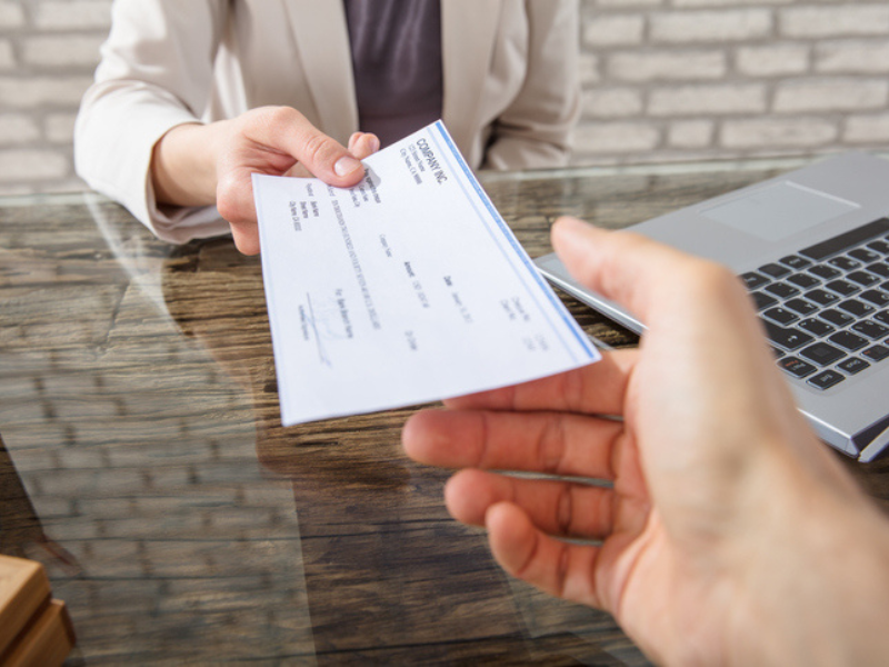A businesswoman hands a cheque to her collegue