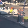 A car guard swinging on a road sign outside a petrol station