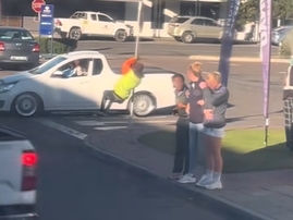 A car guard swinging on a road sign outside a petrol station