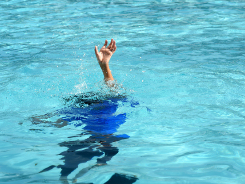 A child holding their hand up in a swimming pool in need of help