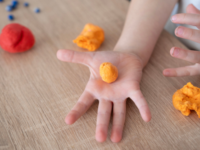 A child holds a ball of playdough in their hands