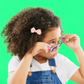 A child looking peaking through half pulled down sunglasses against a green screen