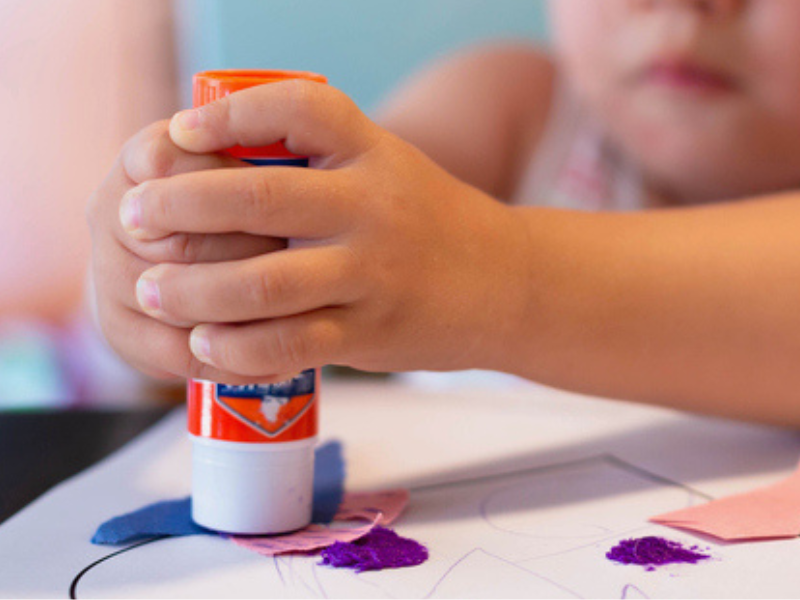 A child using glue stick to stick shape cutouts on paper