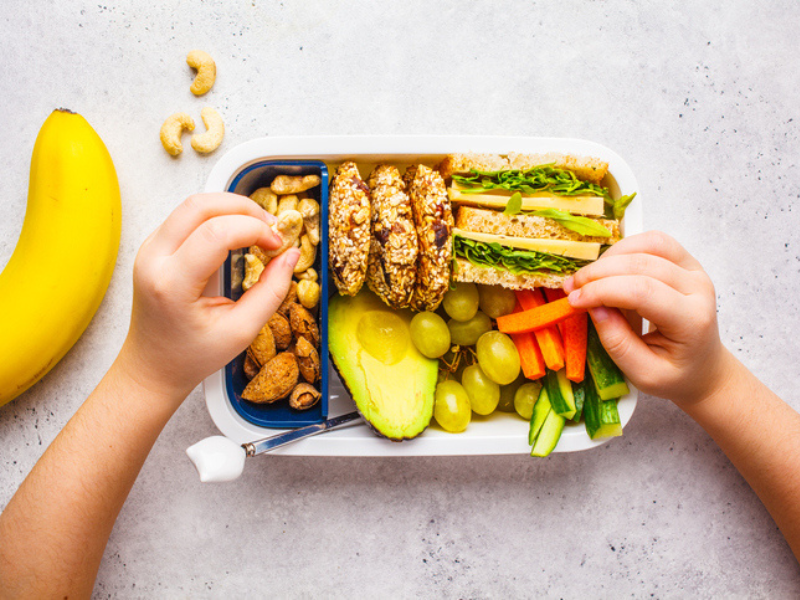 A child's hands eating from a healthy lunch box for school