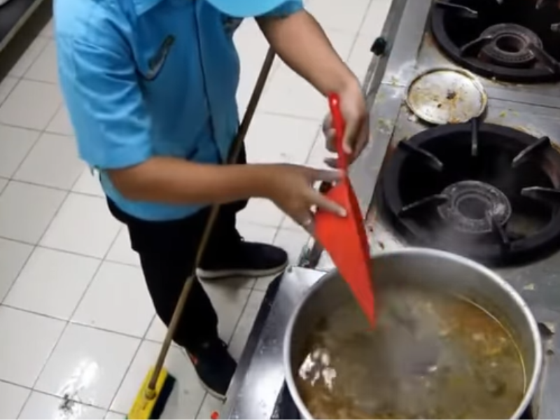 A cleaner drops dirt from a dust pan into a pot of food