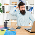 A confused man looks at his laptop scratching his head