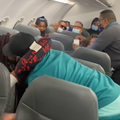 A couple hug on a flight while a passenger is restrained by flight attendant