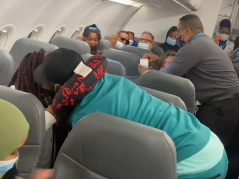 A couple hug on a flight while a passenger is restrained by flight attendant