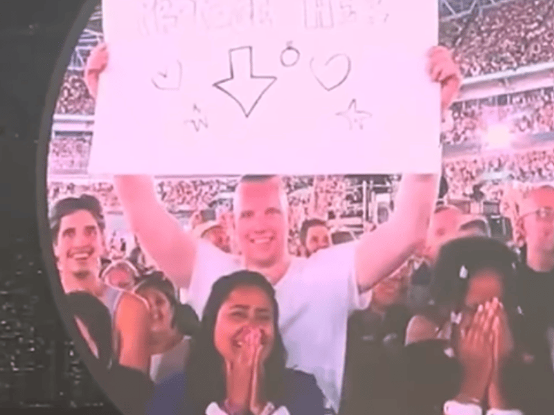 A couple with a sign on the jumbotron at a Coldplay concert
