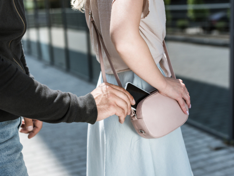 A criminal pickpocketing a smartphone from a womans handbag