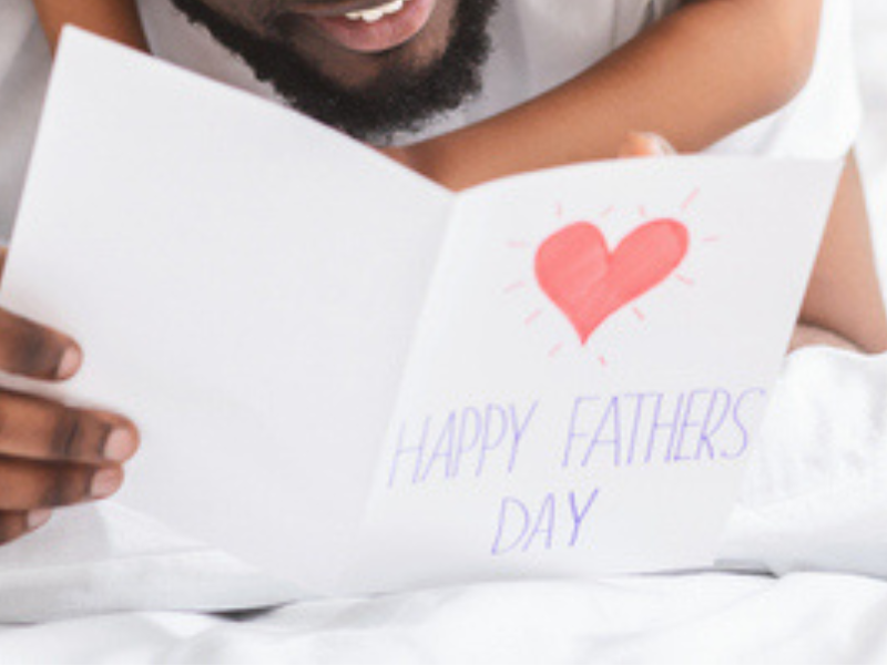 A daughter hangs around her fathers neck as he reads her fathers day card