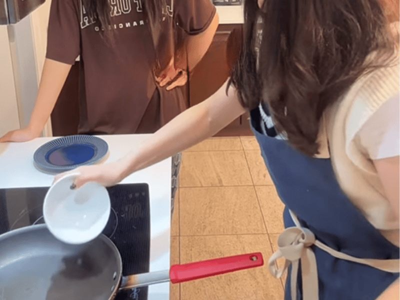 A daughter watches her mother act like shes cooking on the stove