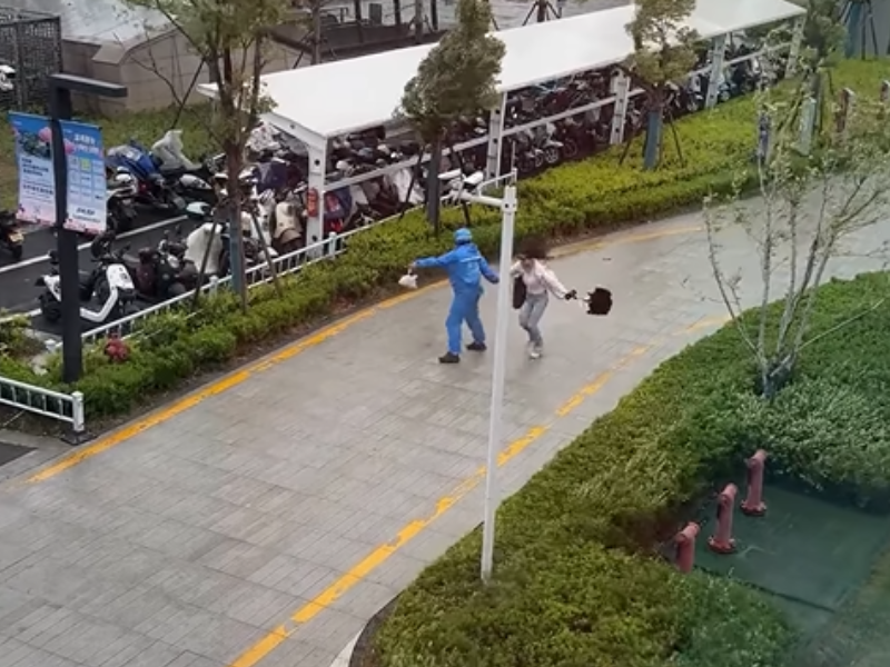A delivery man helps a woman from blowing away in a wind storm