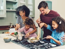 A family of four cooking together in their kitchen at home