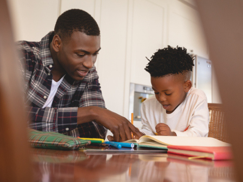 A father does homework with his son at the dining table