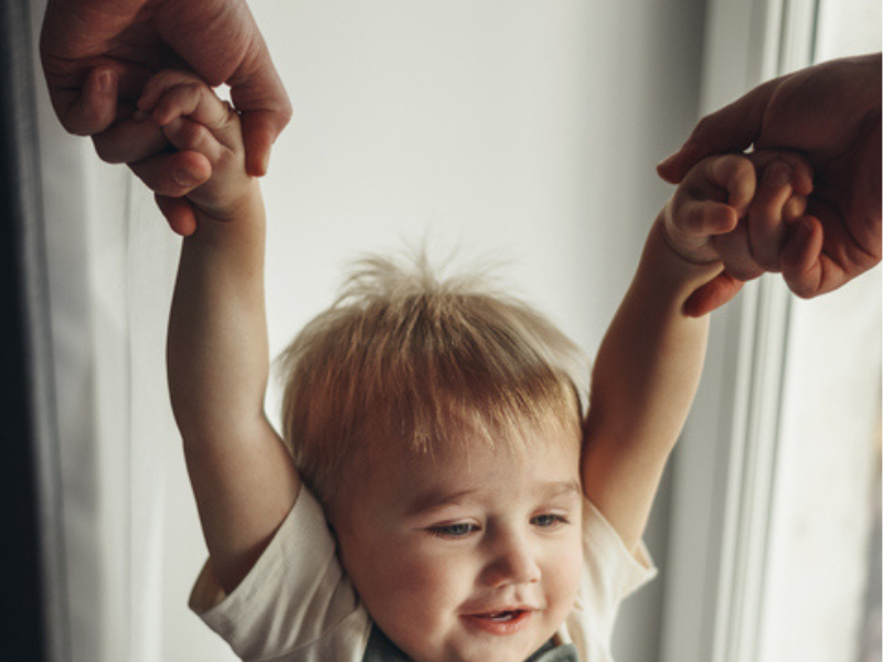 A father pulls his son up by hands at home