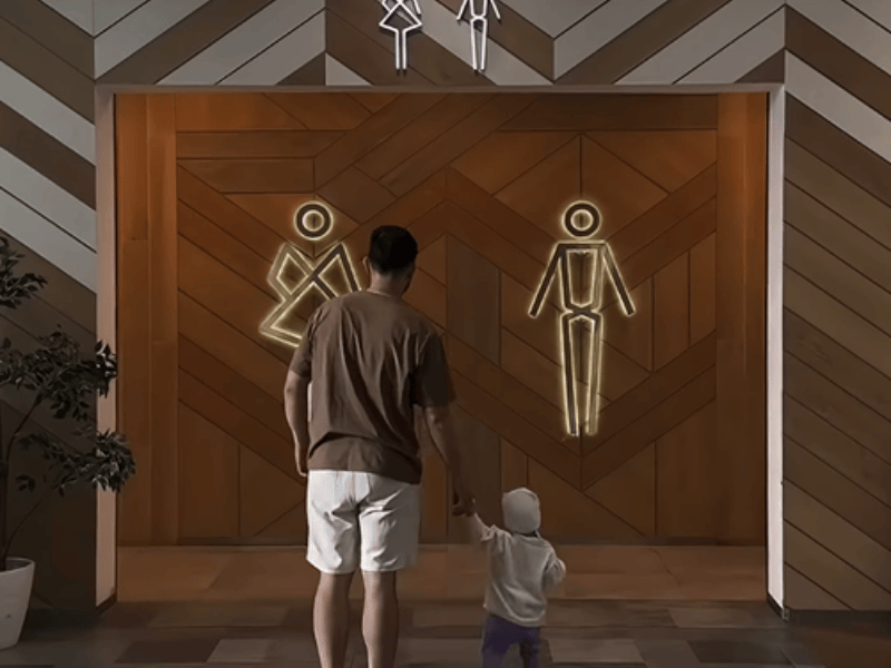 A father stands with his young daughter in front of the public restrooms