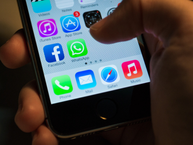 A finger about to click on the WhatsApp icon on a smartphone