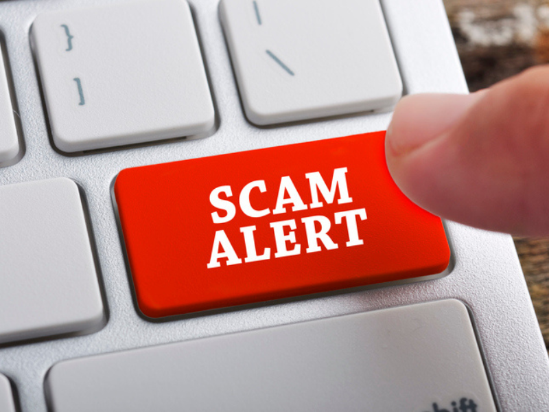 A finger about to press keyboard button that reads scam alert