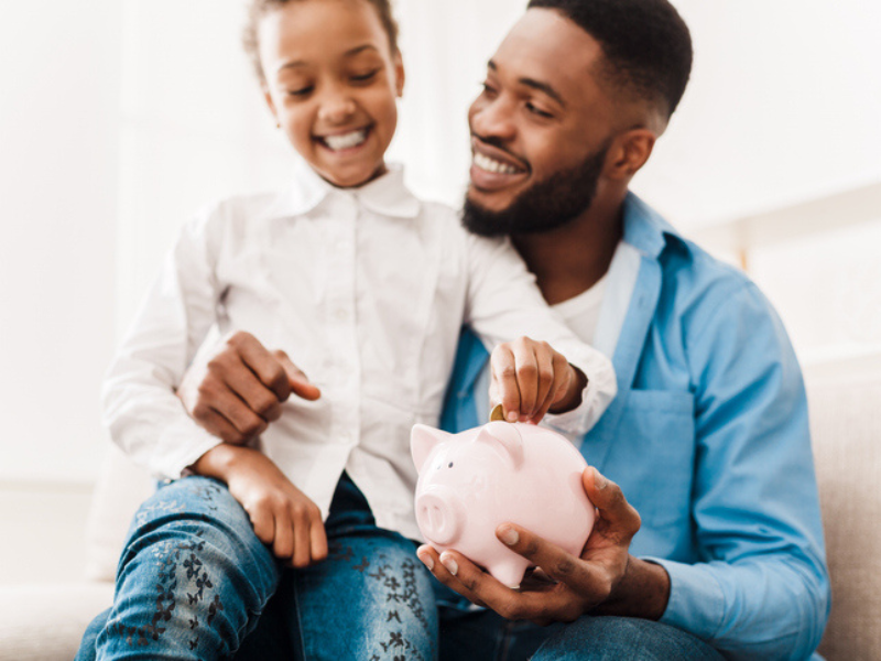 A girl holds a piggy bank with her father