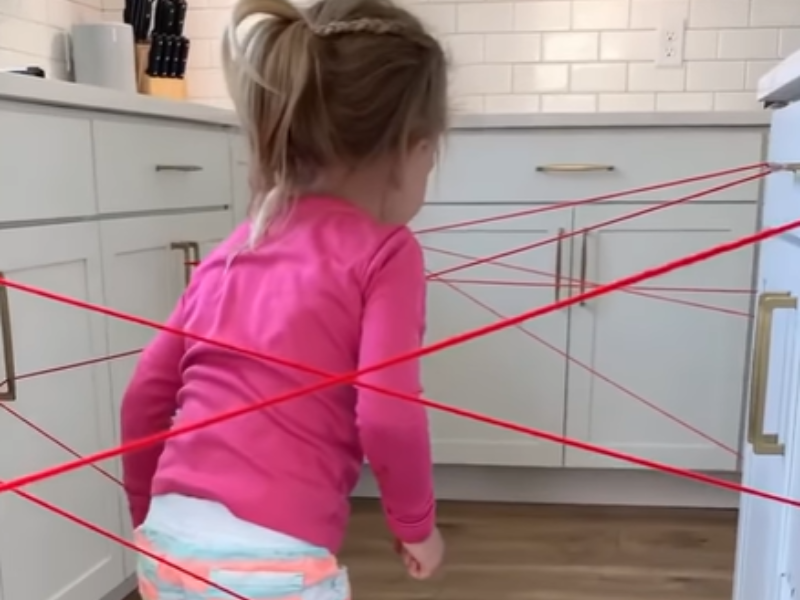 A girl makes her way through a yarn web in the kitchen