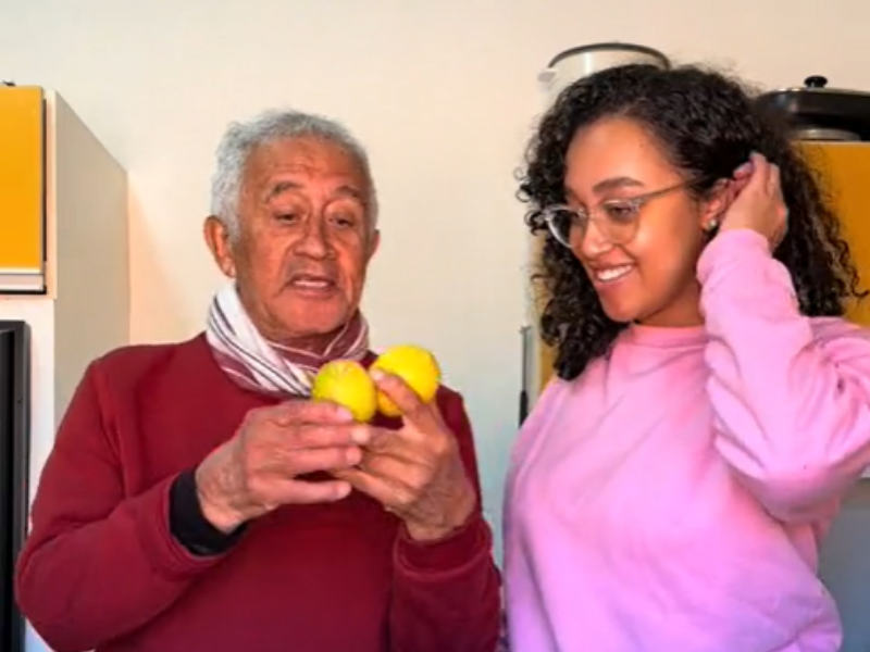 A grandfather holding two lemons standing next to his granddaughter