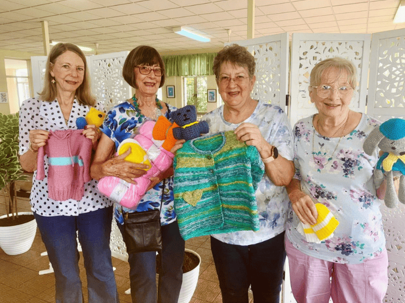 A group of grandmothers holding their handsewn items up for display