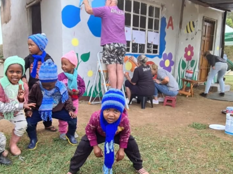 A group of kids play outside a creche that is being painted by volunteers