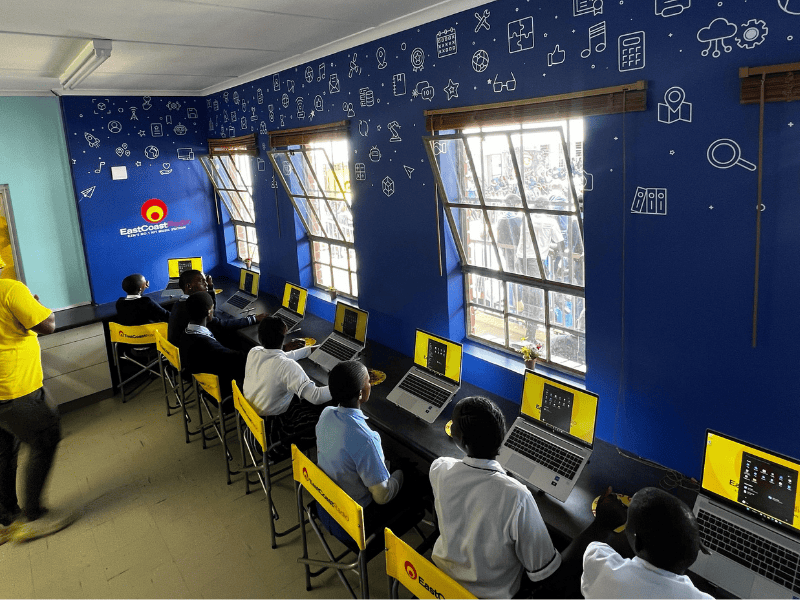 A group of learners sit inside a computer lab with laptops
