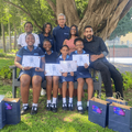 A group of students sit under a tree with their teachers